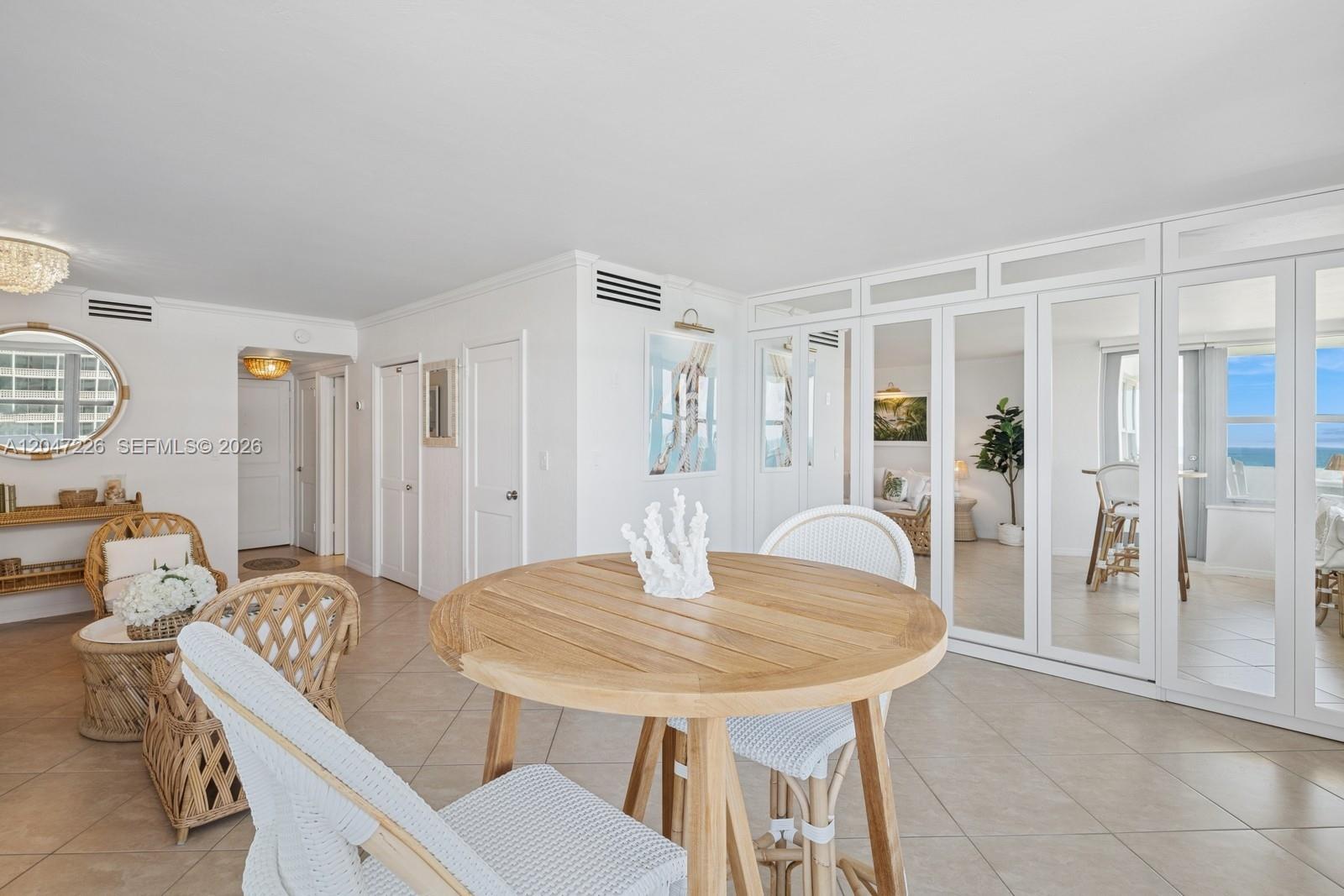 A bright dining area features a wooden table, wicker chairs, and mirrored closet doors — 2899 Collins Ave # 1025, Miami Beach FL 33140, MIAMI BEACH, FL