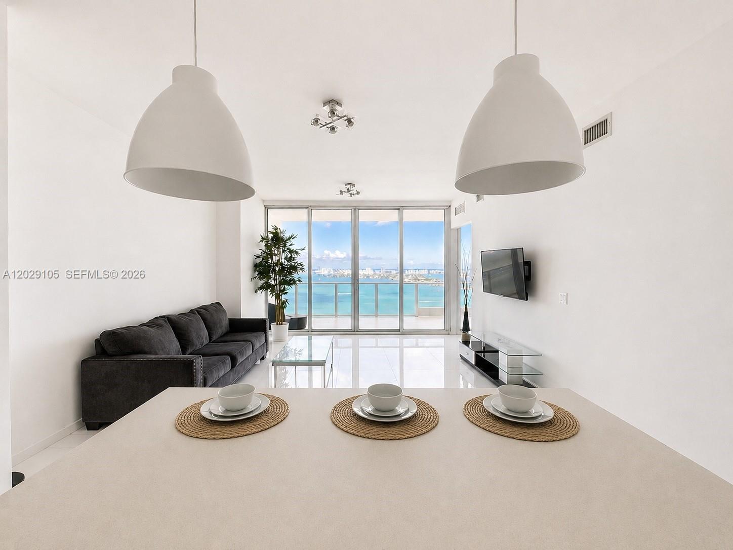A modern living room features white walls, tile floors, a dark sofa, and ocean views — 2020 N Bayshore Dr # 2909, Miami FL 33137, MIAMI, FL