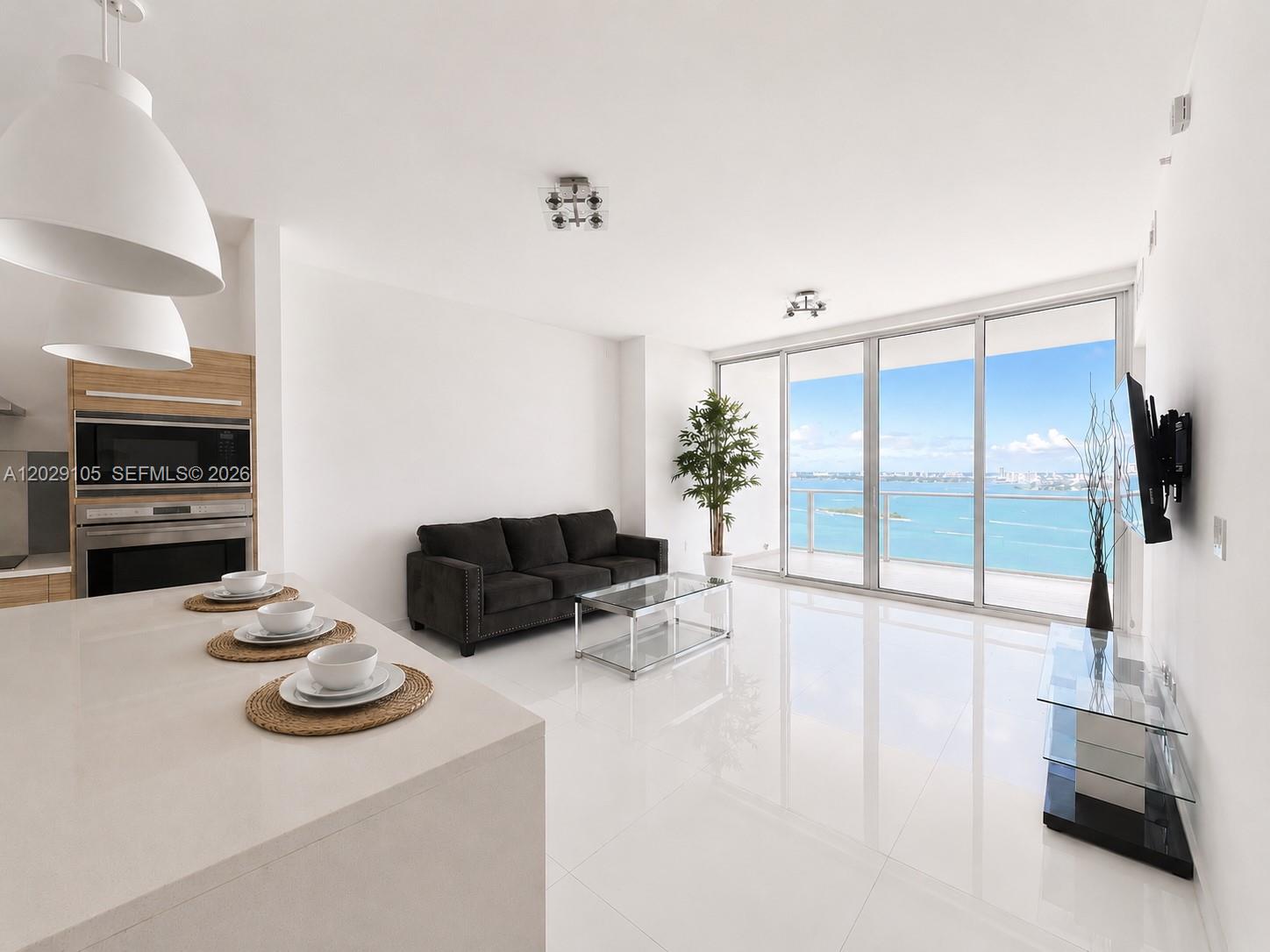 A modern living room and kitchen area features white tile floors and floor-to-ceiling windows — 2020 N Bayshore Dr # 2909, Miami FL 33137, MIAMI, FL