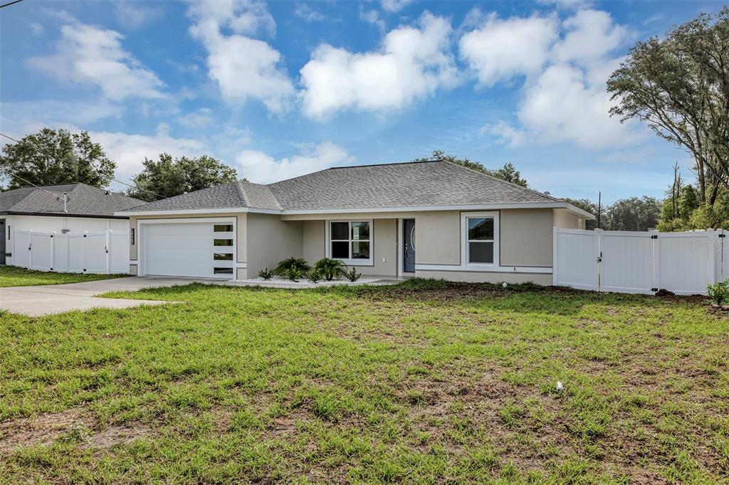 A single-story house with a white garage door, gray roof, and white vinyl fencing — 10463 SW 140TH AVENUE, DUNNELLON, FL