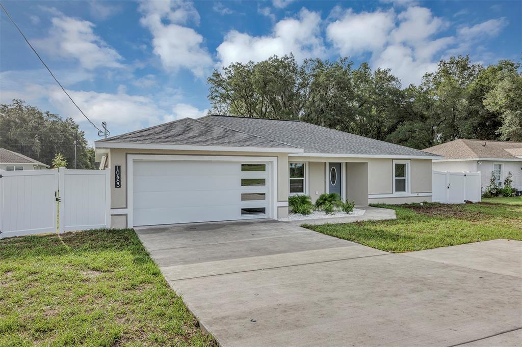 A single-story house with a white garage door, light-colored stucco exterior, and a concrete driveway — 10463 SW 140TH AVENUE, DUNNELLON, FL