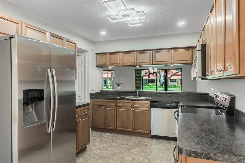 A kitchen with wood cabinets, stainless steel appliances, dark countertops, and a window view — 8235 AMBROSE COVE WAY, ORLANDO, FL