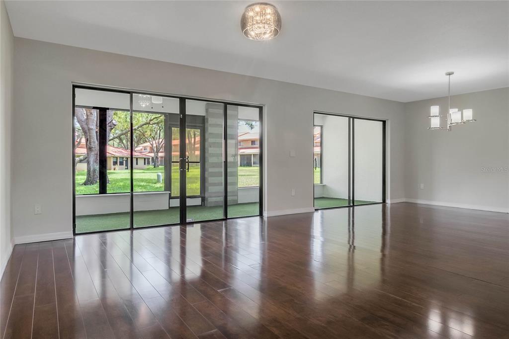 A spacious room with dark hardwood floors, large glass doors, and a view of greenery — 8235 AMBROSE COVE WAY, ORLANDO, FL