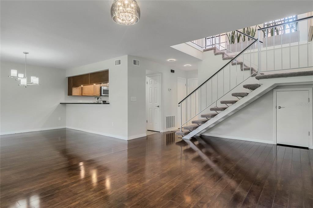 A living area features dark hardwood floors, a staircase with metal railings, and an open kitchen — 8235 AMBROSE COVE WAY, ORLANDO, FL