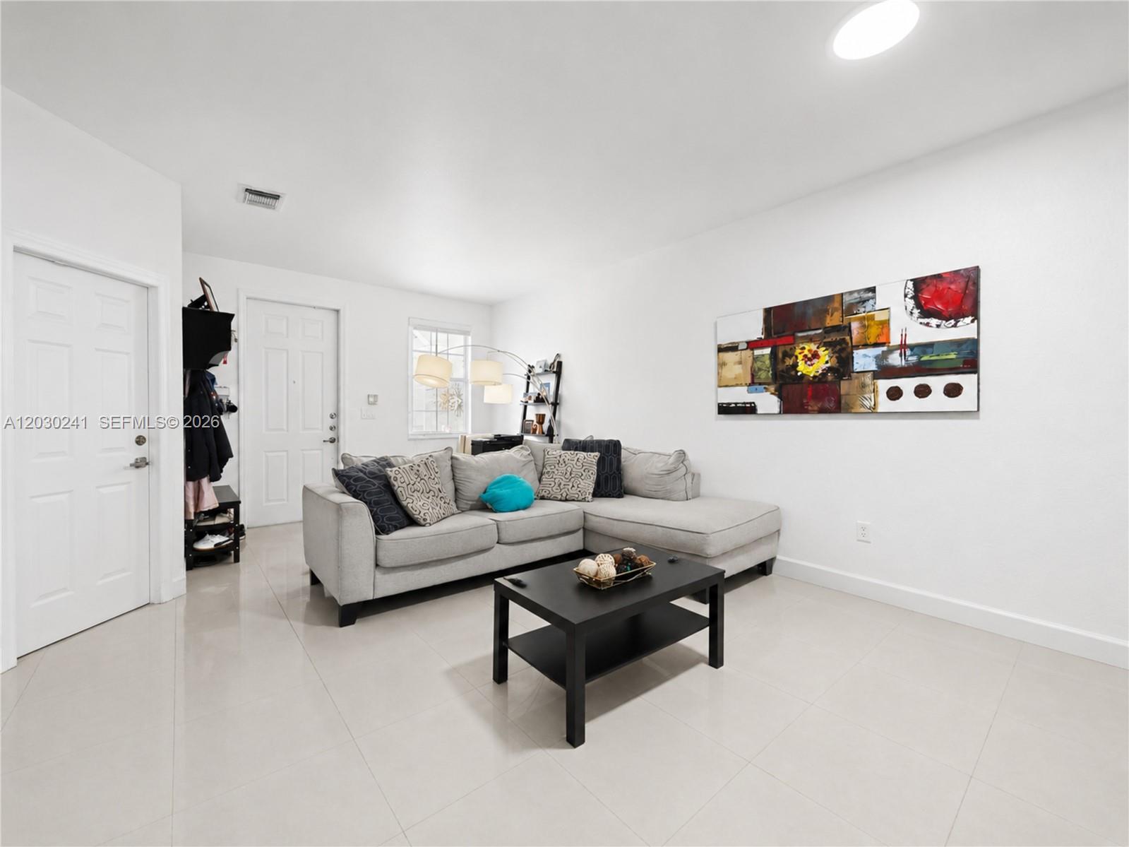 A living room features a grey sectional sofa, a black coffee table, and abstract wall art — 10918 NW 78th Ter, Doral FL 33178, DORAL, FL