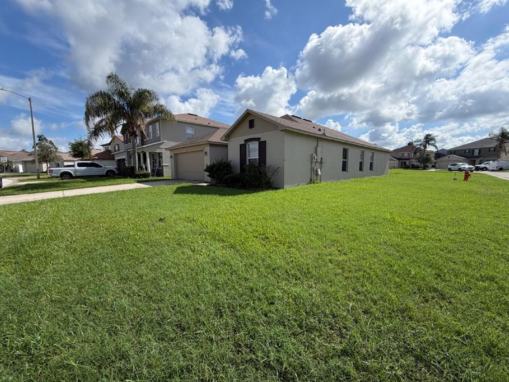 A single-story house with a beige exterior and a two-car garage sits on a lawn — 1153 ELDERBERRY DRIVE, DAVENPORT, FL