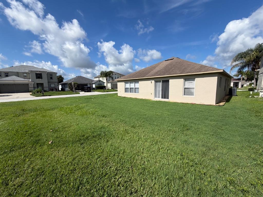 The exterior rear view of a tan single-story house with a lawn and neighboring homes — 1153 ELDERBERRY DRIVE, DAVENPORT, FL