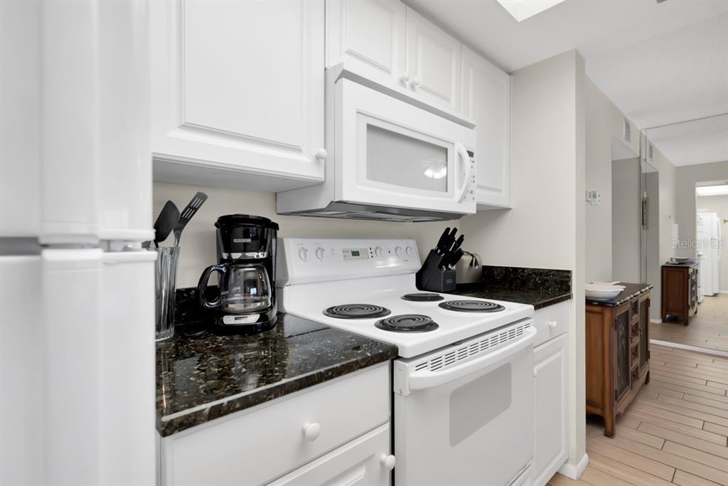 A kitchen features white cabinets, a white stove, a microwave, and dark granite countertops — 2312 GULF DRIVE N UNIT 103, BRADENTON BEACH, FL