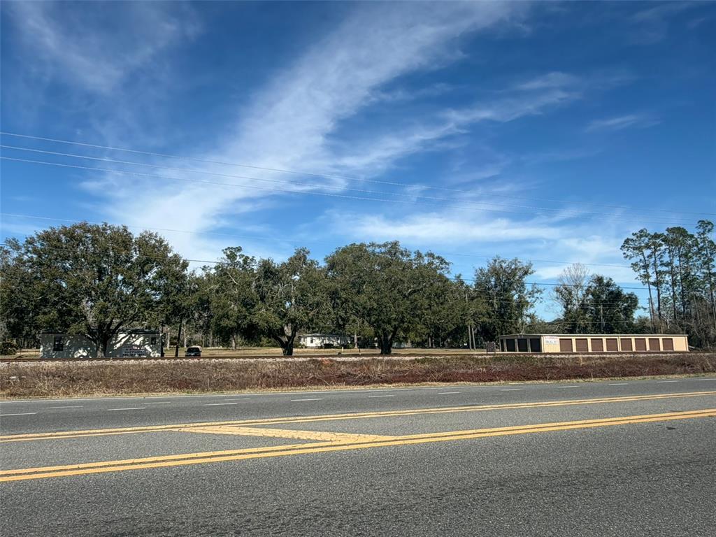 A view of a grassy lot with trees and storage units behind a paved road — 12776 RAILROAD STREET, LIVE OAK, FL