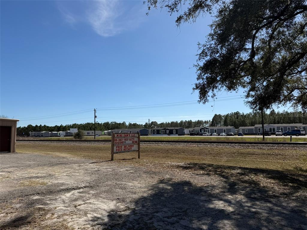 A gravel lot features a small business sign in front of a railroad track and homes — 12776 RAILROAD STREET, LIVE OAK, FL