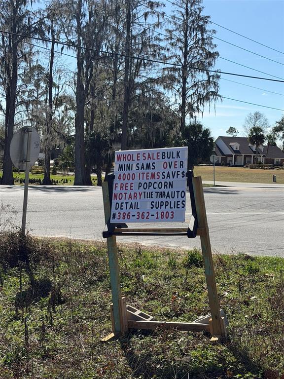 A portable sign stands on a grassy roadside advertising a business with a phone number — 12776 RAILROAD STREET, LIVE OAK, FL