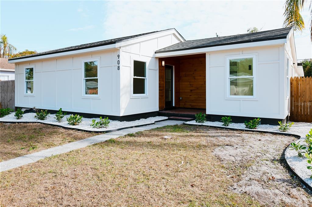 A single-story house with white board-and-batten siding, a wood-paneled entryway, and white landscaping rocks — 908 61ST STREET S, GULFPORT, FL