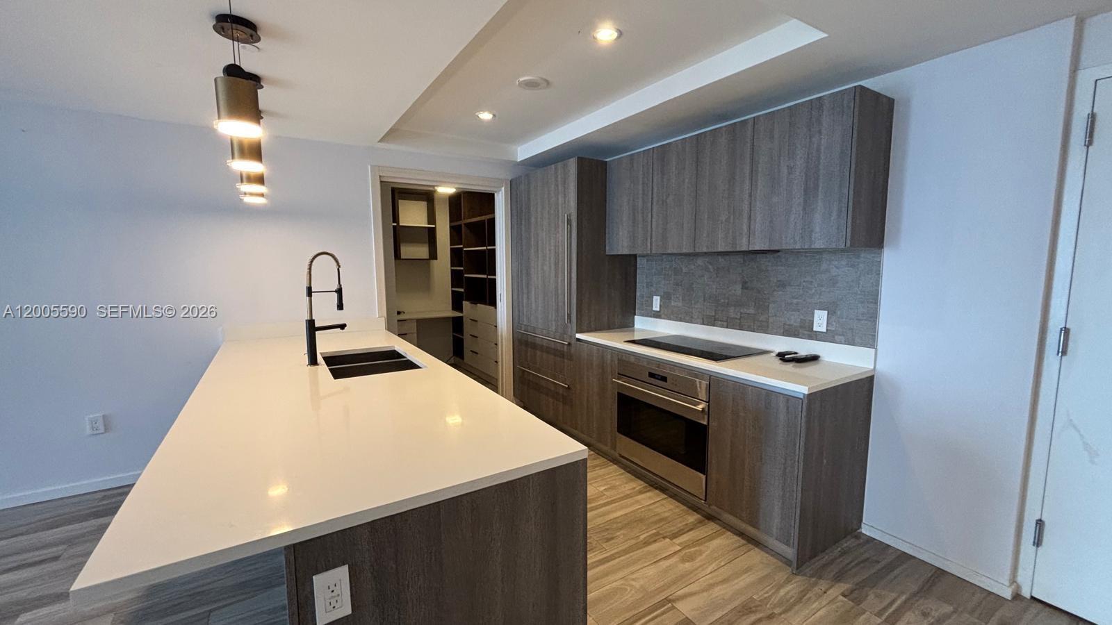 A modern kitchen features dark wood cabinetry, white countertops, and a central island — 801 S Miami Ave # 3510, Miami FL 33130, MIAMI, FL