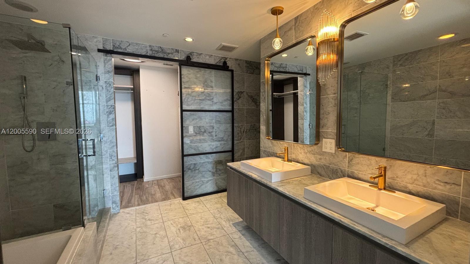 A modern bathroom features a double vanity, marble tile walls, and a sliding glass door — 801 S Miami Ave # 3510, Miami FL 33130, MIAMI, FL