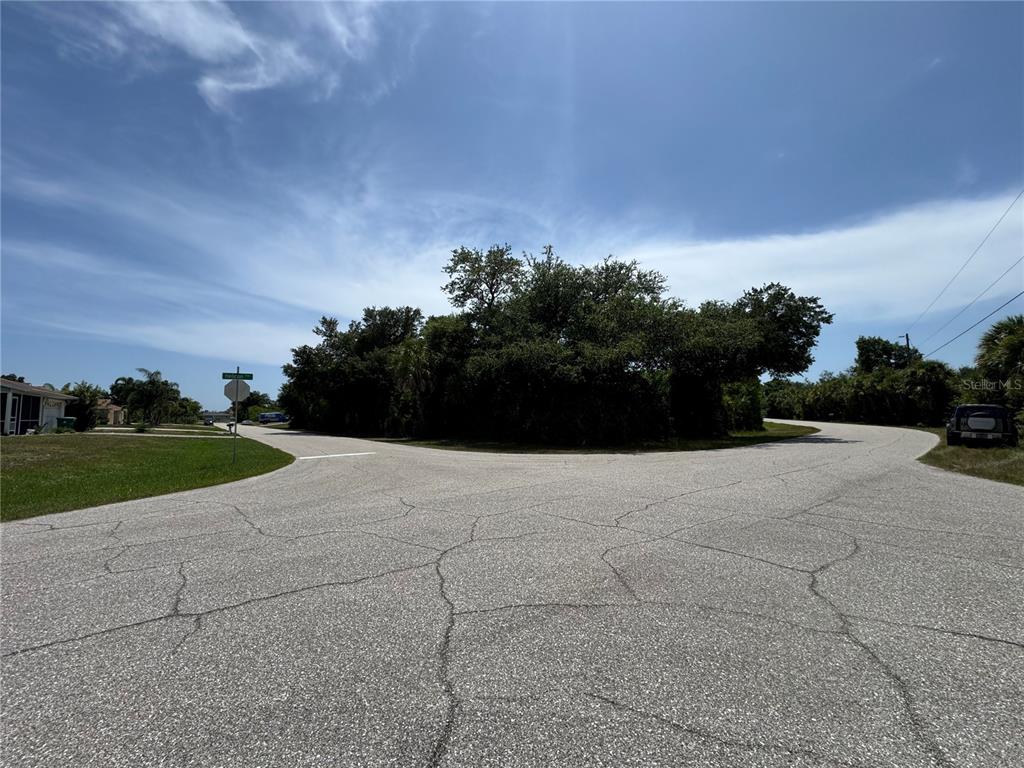 A paved road forks in front of a wooded lot under a blue sky — 7251 FINNEGAN STREET, PORT CHARLOTTE, FL