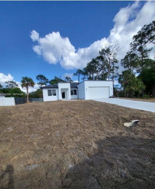A modern, single-story white house with a two-car garage stands on a dirt lot — 718 Robert Ave, Lehigh Acres FL 33936, LEHIGH ACRES, FL