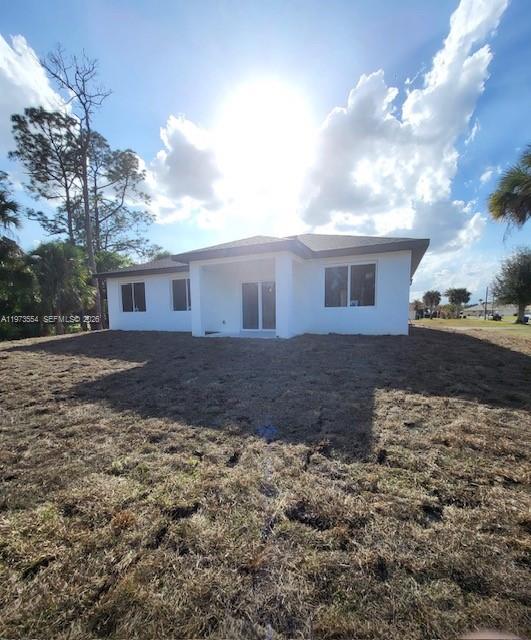 The exterior of a white, single-story house with a yard under a sunny sky — 718 Robert Ave, Lehigh Acres FL 33936, LEHIGH ACRES, FL
