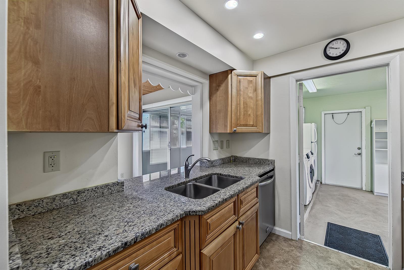 A kitchen features wood cabinets, granite countertops, a double sink, and an adjacent laundry room — 2581 E Golf Boulevard, Pompano Beach FL 33064, POMPANO BEACH, FL