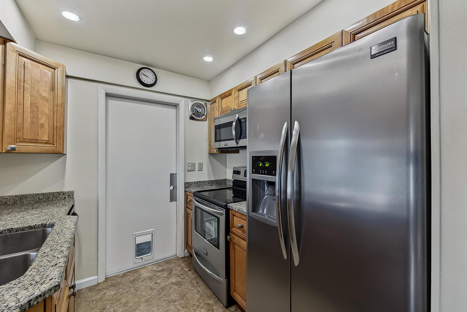 A kitchen features stainless steel appliances, wood cabinets, granite countertops, and a door with a pet door — 2581 E Golf Boulevard, Pompano Beach FL 33064, POMPANO BEACH, FL
