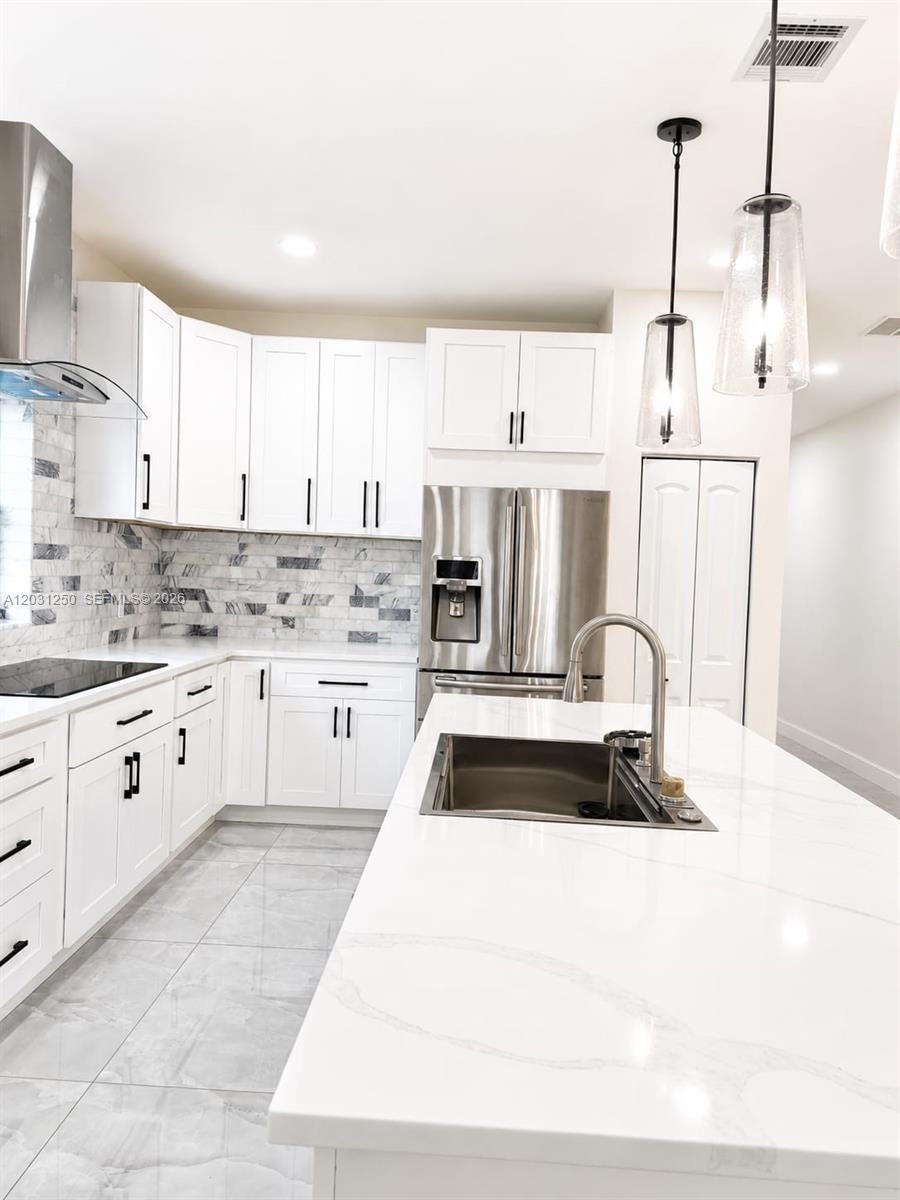 A modern kitchen features white cabinets, marble-style backsplash, stainless steel appliances, and a quartz island — 907 21st St, West Palm Beach FL 33407, WEST PALM BEACH, FL