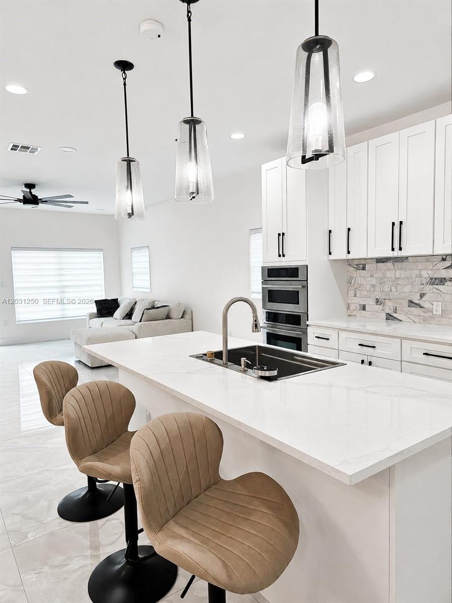A modern kitchen features a white quartz island, pendant lighting, and tan bar stools — 907 21st St, West Palm Beach FL 33407, WEST PALM BEACH, FL