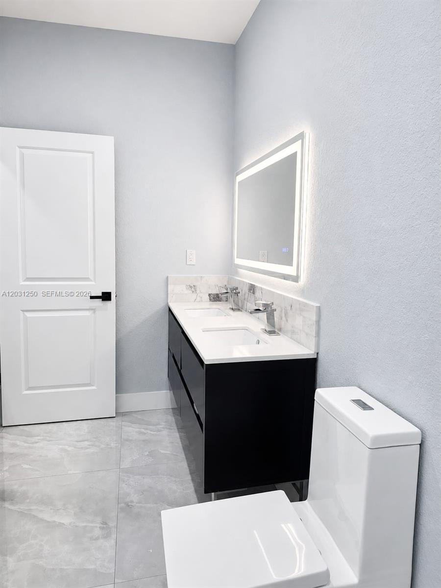 A modern bathroom features a double vanity with a backlit mirror and gray tile flooring — 907 21st St, West Palm Beach FL 33407, WEST PALM BEACH, FL