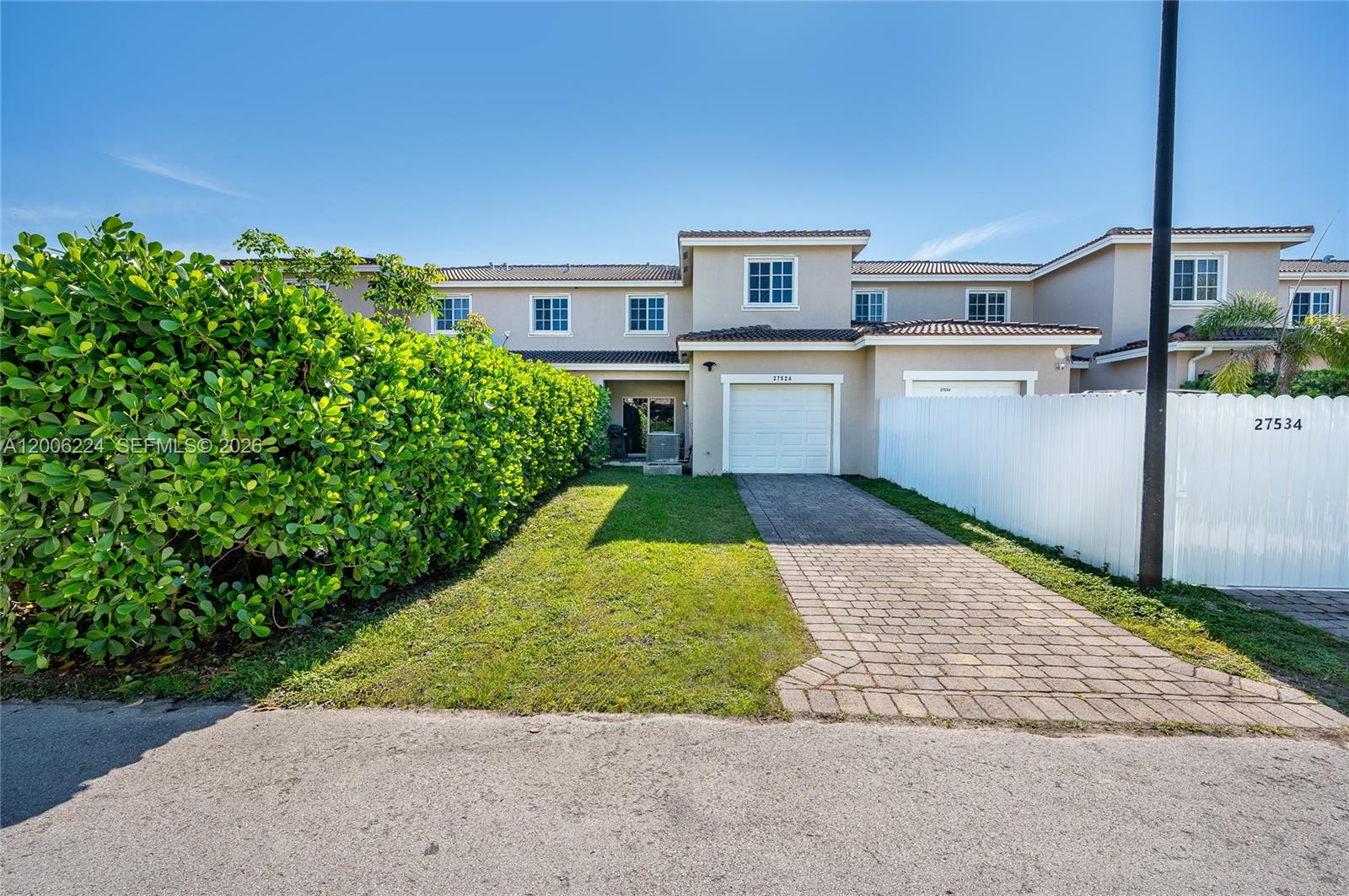 A two-story townhouse features a paved driveway, a white fence, and a large hedge — 27524 SW 140th Ave, Homestead FL 33032, HOMESTEAD, FL