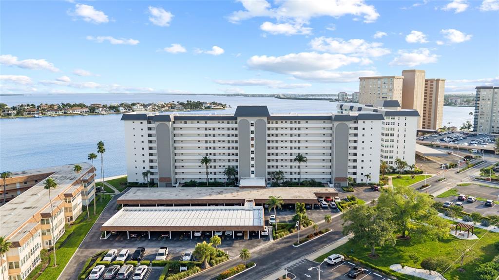 An aerial view shows a multi-story apartment building with a covered parking structure and waterfront — 5108 BRITTANY DRIVE S UNIT 903, ST PETERSBURG, FL