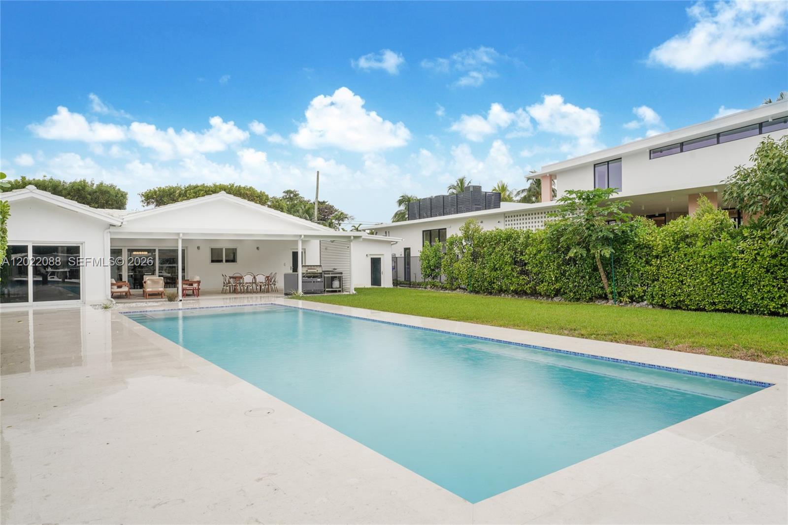 A rectangular swimming pool sits in front of a white house with a covered patio — 801 NE 76th St, Miami FL 33138, MIAMI, FL