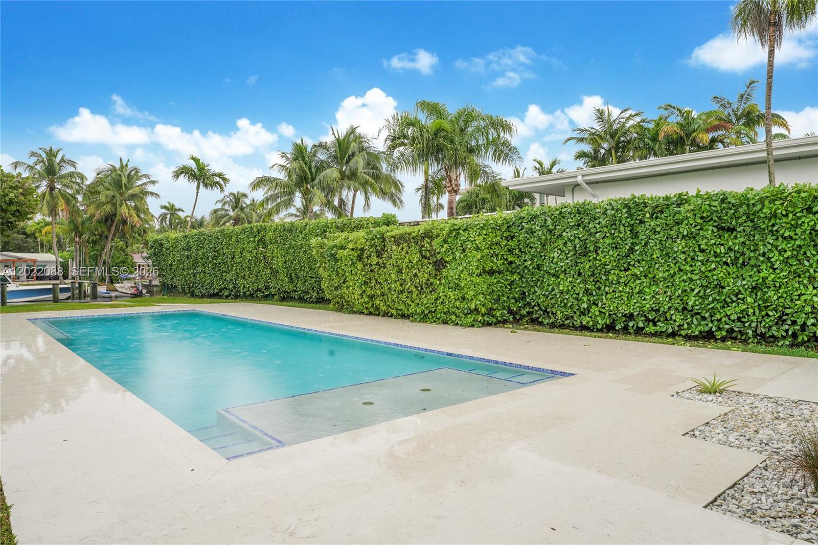 A rectangular swimming pool with a shallow sun shelf sits on a patio beside hedges — 801 NE 76th St, Miami FL 33138, MIAMI, FL