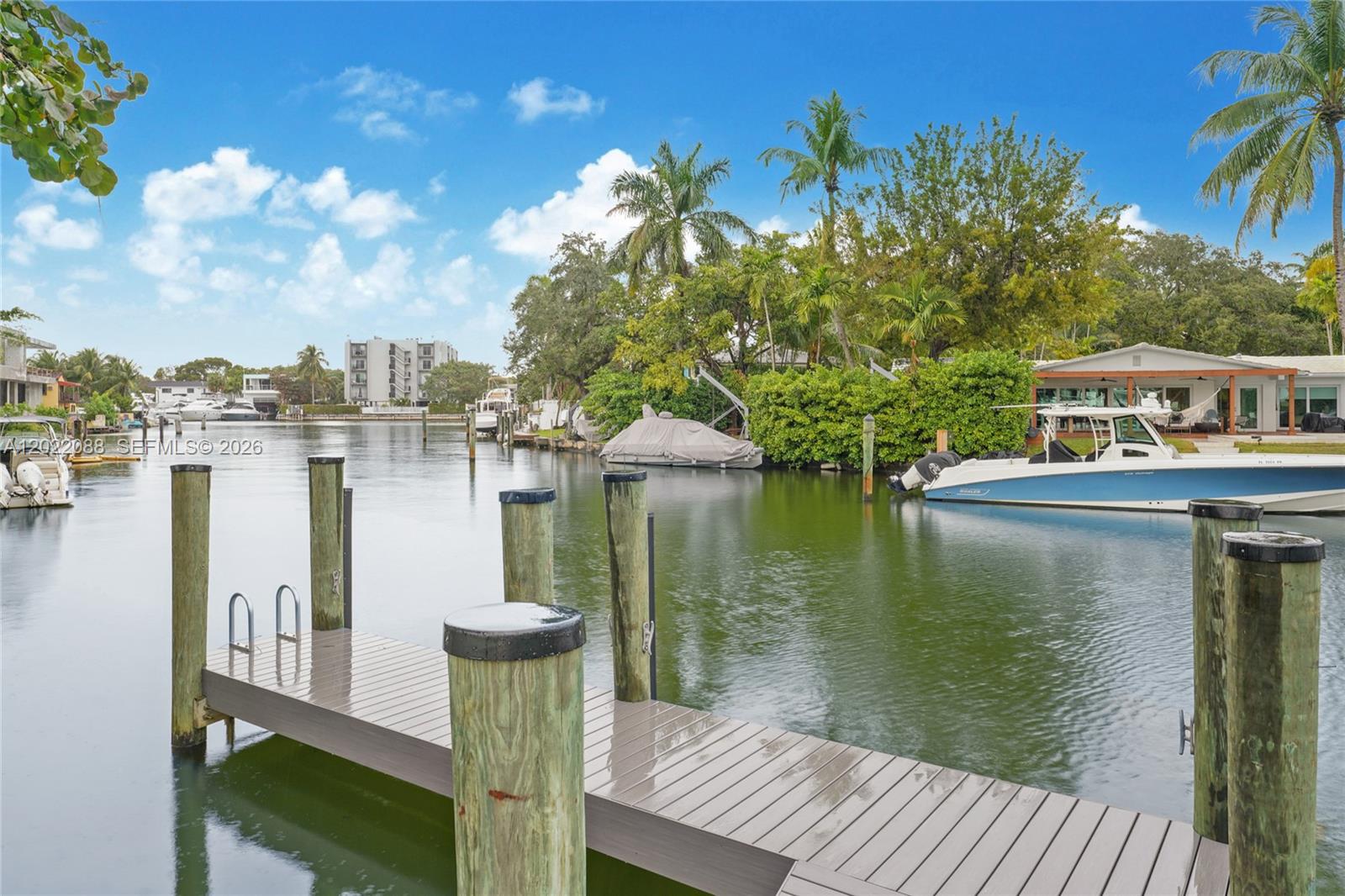 A wooden dock extends into a canal with boats moored along the grassy banks — 801 NE 76th St, Miami FL 33138, MIAMI, FL
