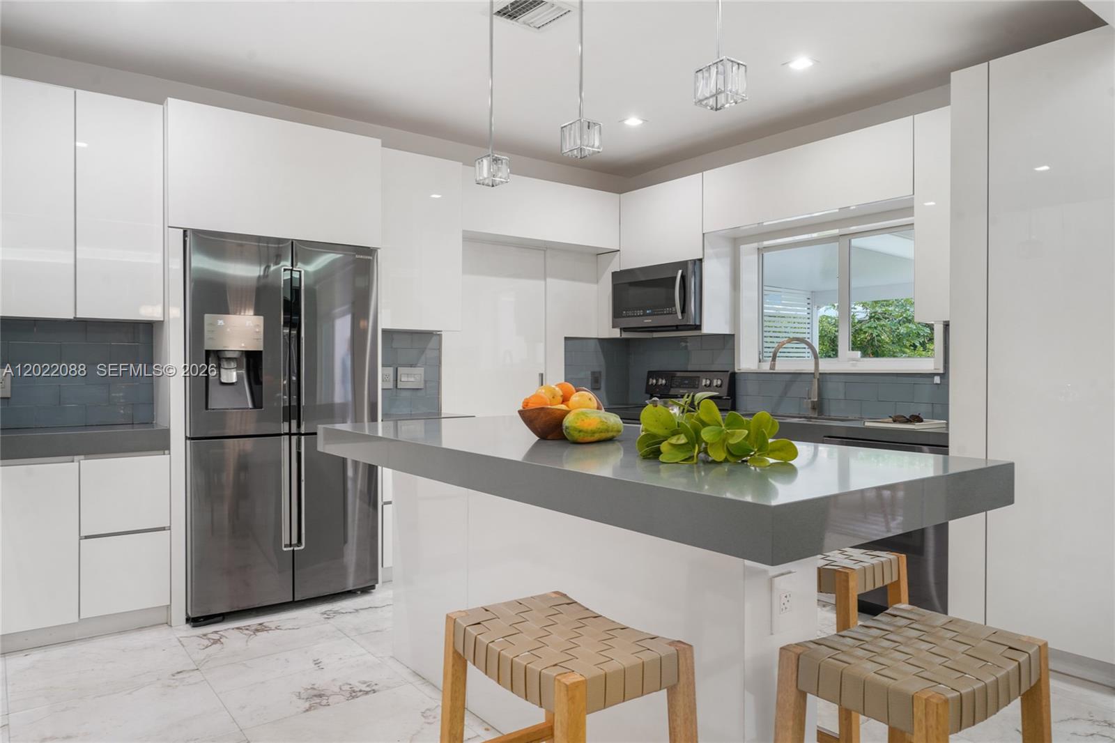 A modern kitchen features white cabinets, a gray island, stainless steel appliances, and tile flooring — 801 NE 76th St, Miami FL 33138, MIAMI, FL