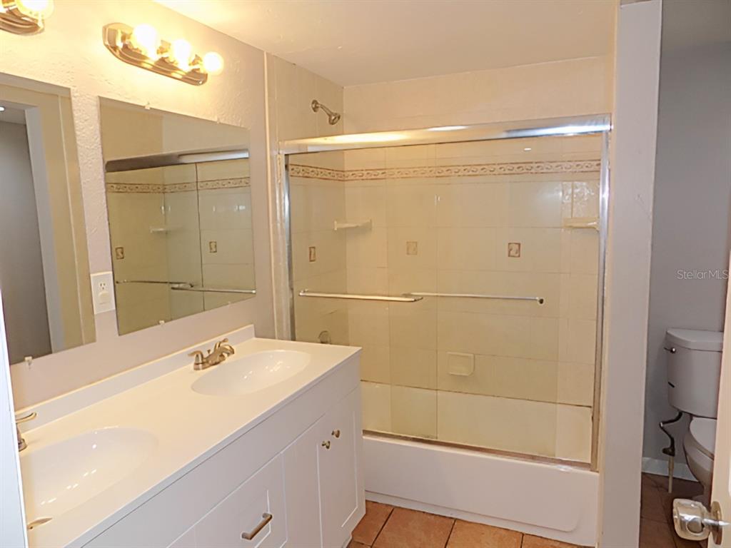 A bathroom features a double vanity with white cabinets, a mirror, and a shower-tub combo — 4610 SLOAN AVENUE, SARASOTA, FL