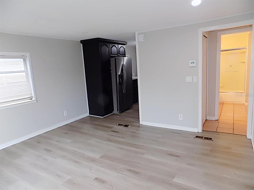 A room with light wood-look flooring, gray walls, a black refrigerator, and a bathroom doorway — 4610 SLOAN AVENUE, SARASOTA, FL