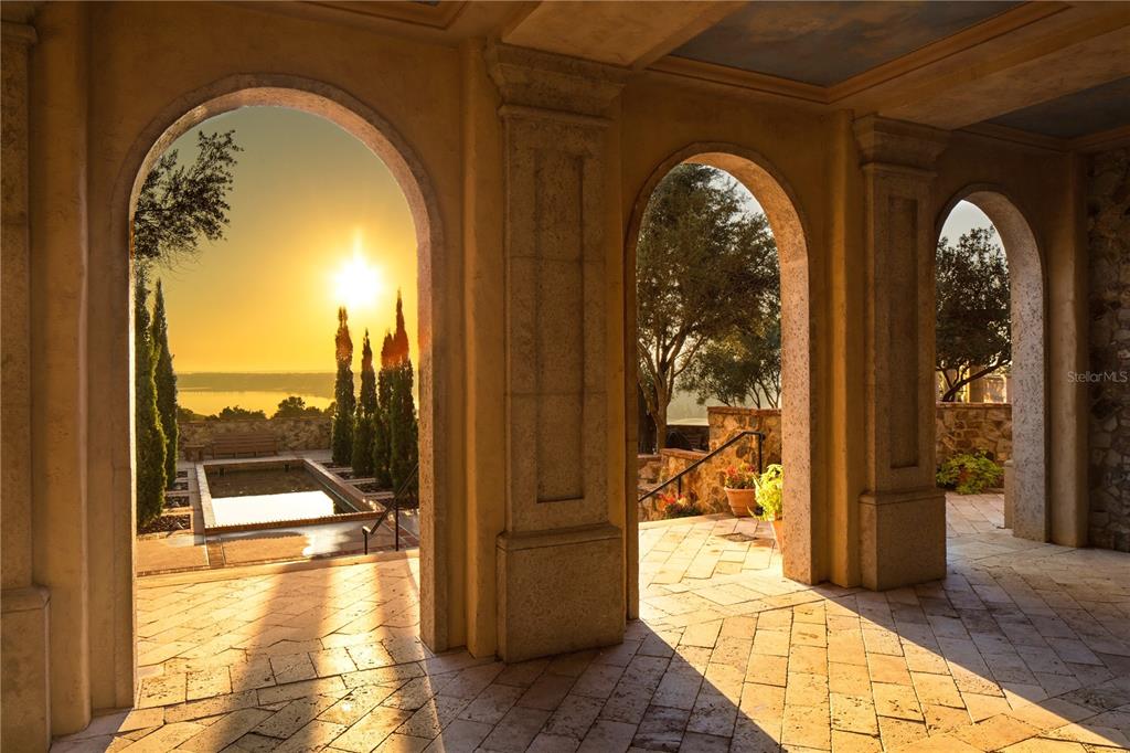 A stone-tiled loggia with arched openings overlooks a sunset view of a pool and lake — 15393 APENNINE WAY, MONTVERDE, FL