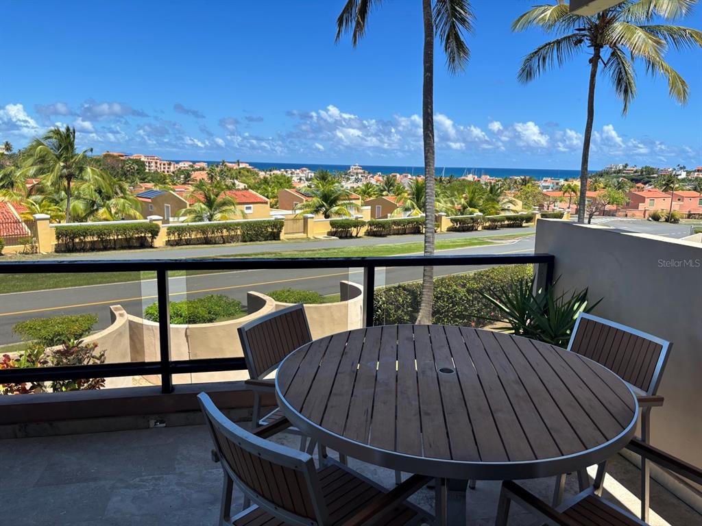A balcony with a round wooden table and chairs overlooks a road and the ocean — 170 PALMAS DRIVE UNIT C3, HUMACAO, PR
