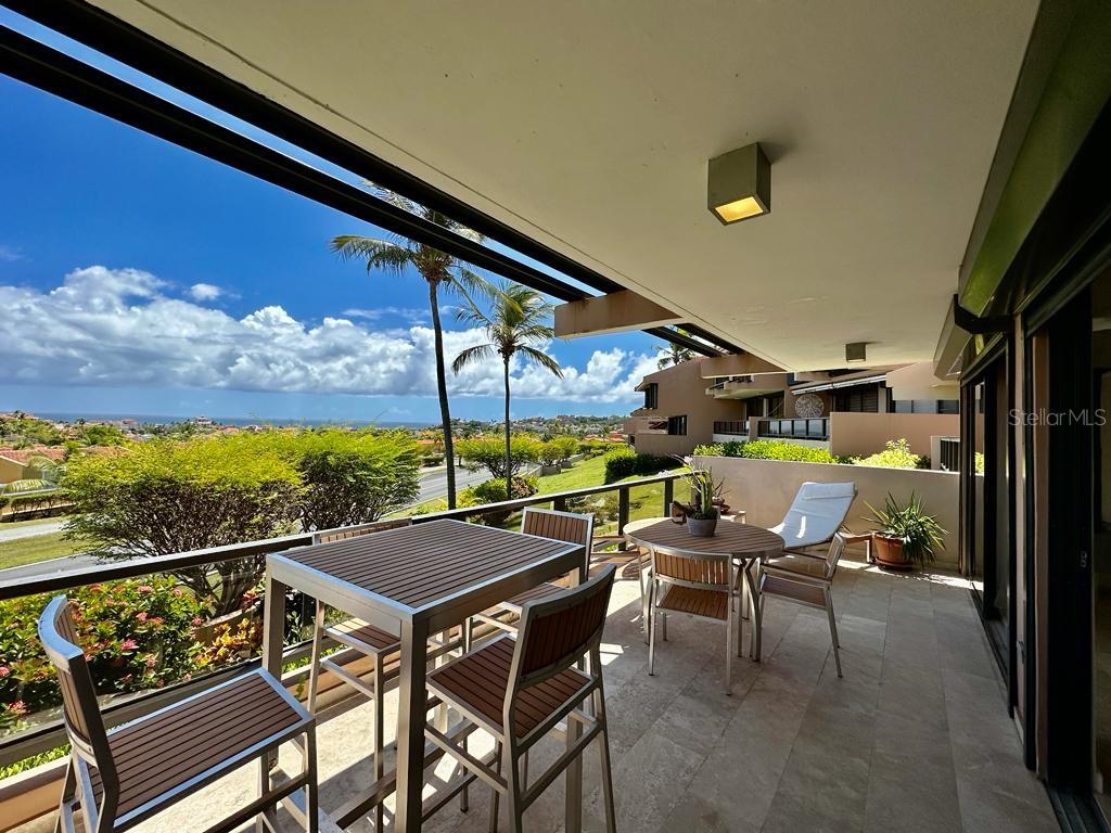 A covered balcony features a dining set, lounge chairs, stone flooring, and ocean views — 170 PALMAS DRIVE UNIT C3, HUMACAO, PR