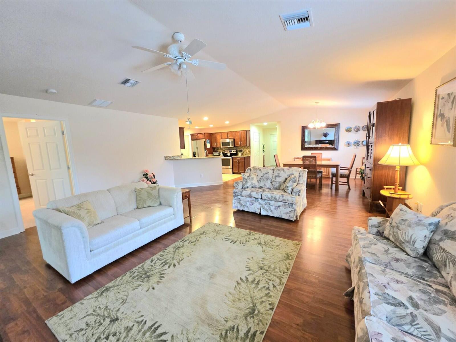 A living room with hardwood floors, a floral sofa, and an open kitchen in the background — 17 San Felipe, Fort Pierce FL 34951, FORT PIERCE, FL