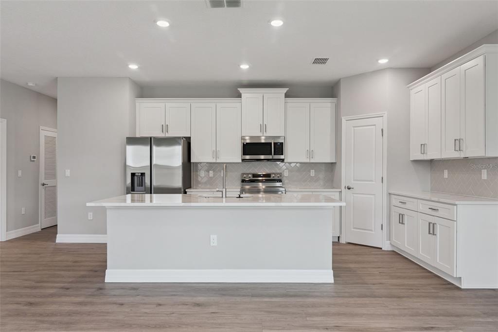 A modern kitchen features white cabinetry, stainless steel appliances, a center island, and wood-look flooring — 3694 SW 131ST STREET, OCALA, FL