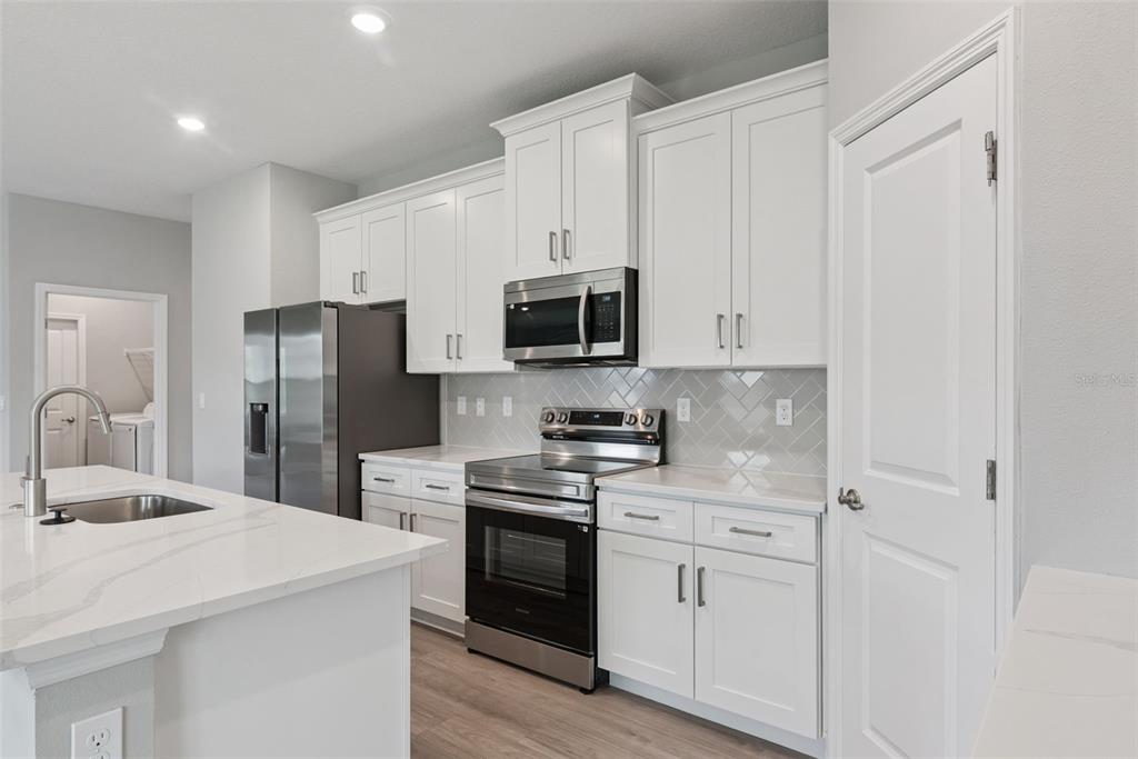 A modern kitchen features white cabinets, stainless steel appliances, and a quartz-topped island — 3694 SW 131ST STREET, OCALA, FL