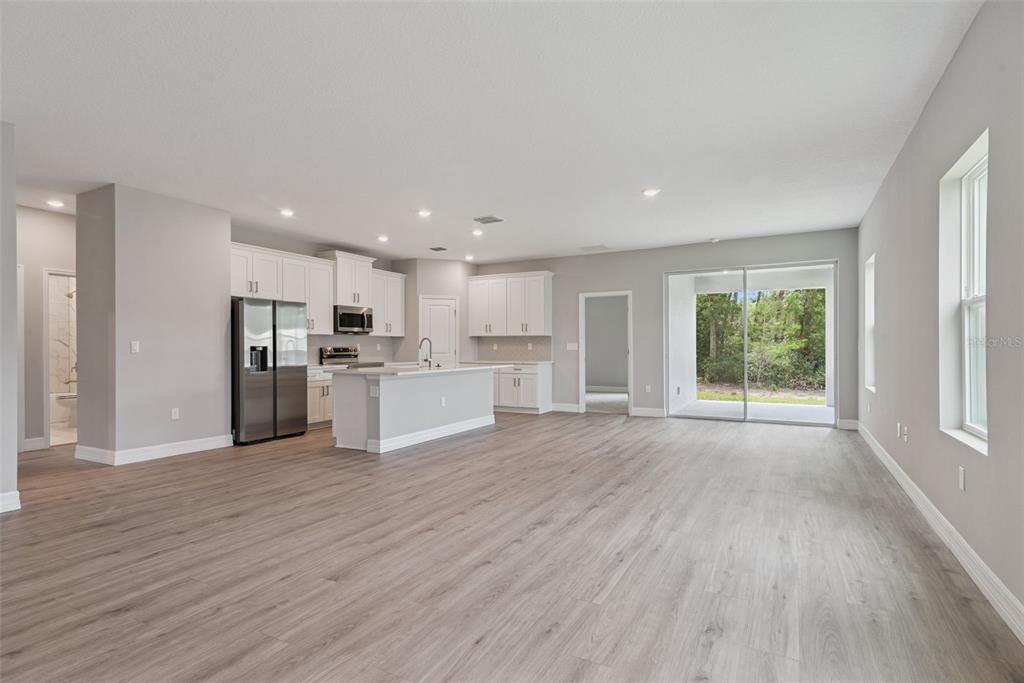 A kitchen with white cabinets and an island opens into a living area with flooring — 3694 SW 131ST STREET, OCALA, FL