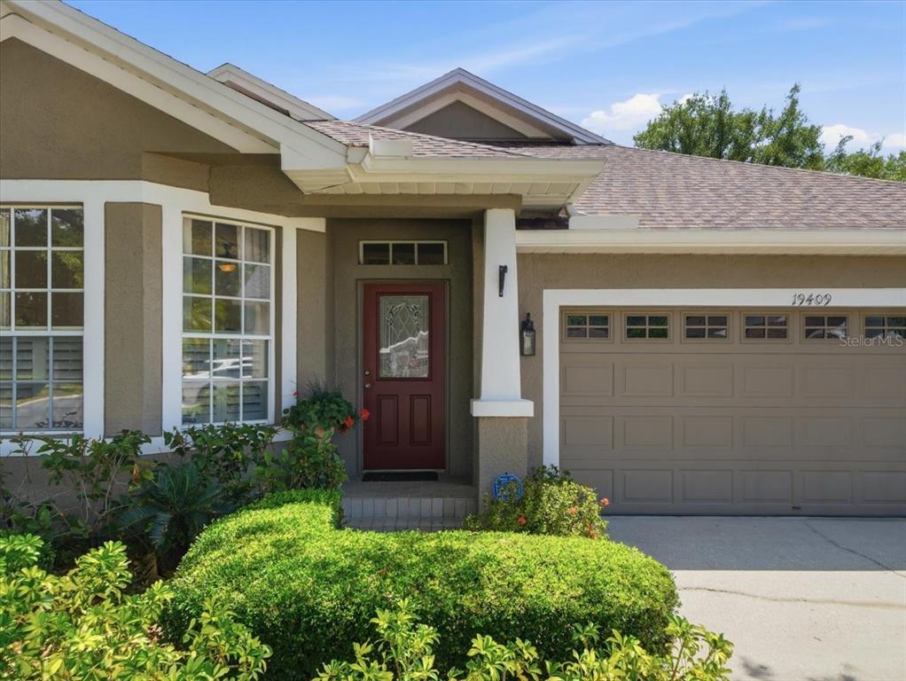 A tan house exterior features a red front door, a garage, and a landscaped yard — 19409 GOLDEN SLIPPER PLACE, LUTZ, FL