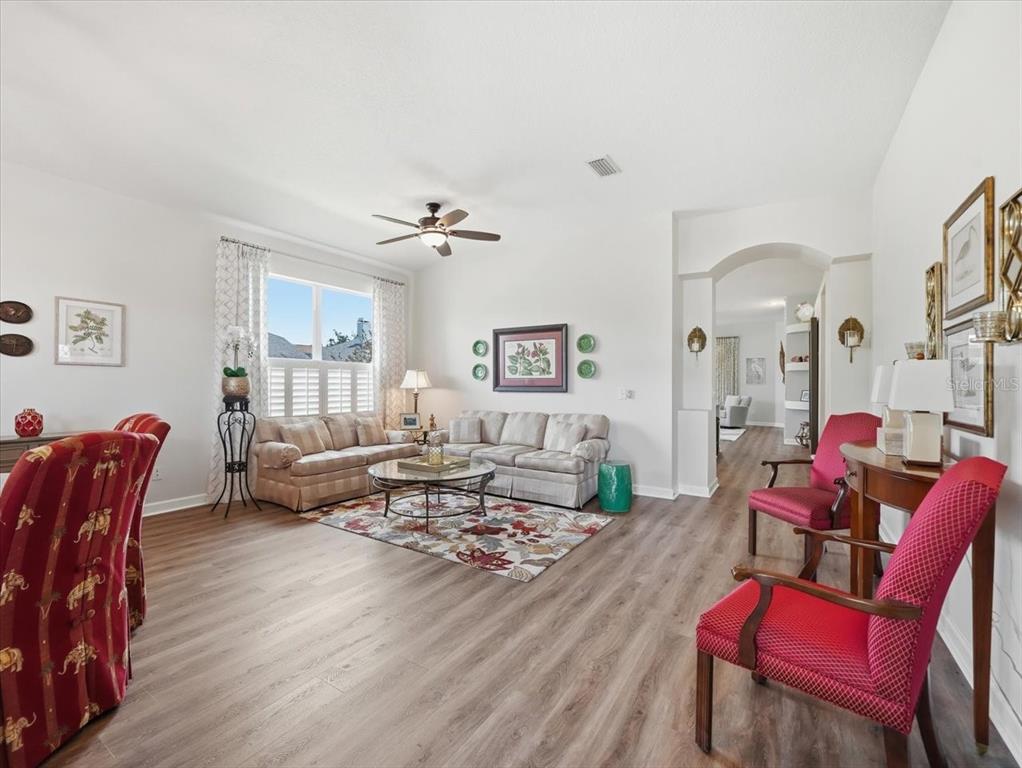 A living room with wood-look flooring, a ceiling fan, and red upholstered chairs — 19409 GOLDEN SLIPPER PLACE, LUTZ, FL