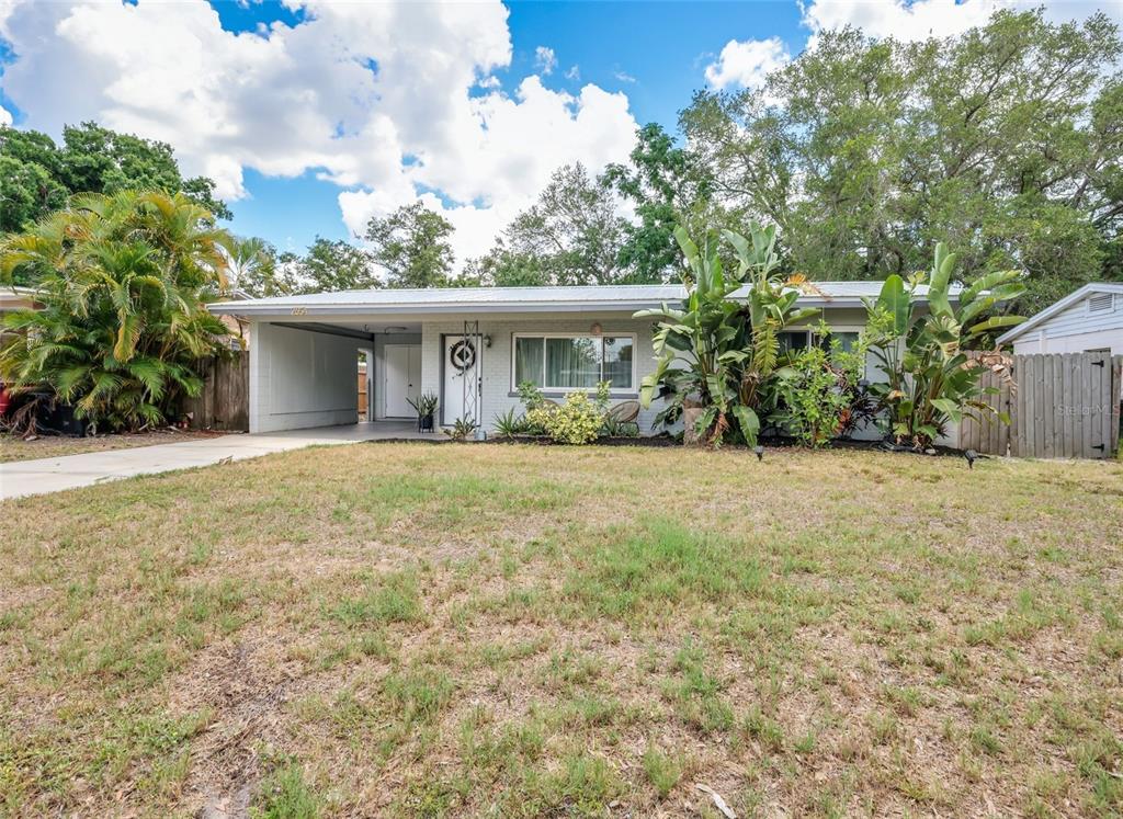 A single-story house with a carport, white brick facade, and large tropical plants in front — 2654 GRAND CAYMAN STREET, SARASOTA, FL