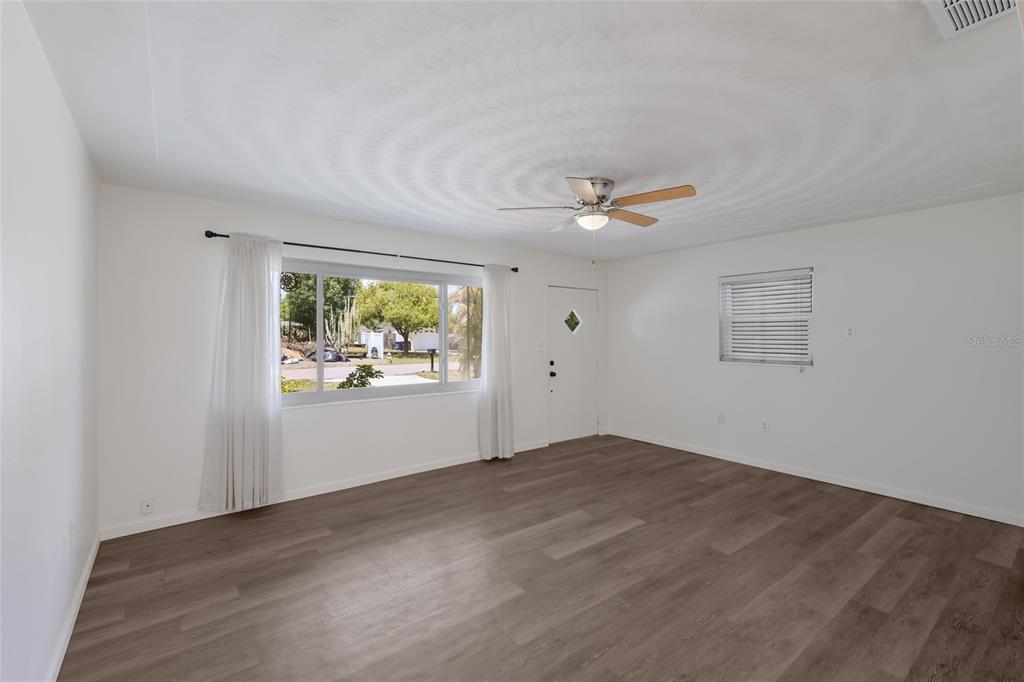 A living room with white walls, wood-look flooring, a ceiling fan, and a large window — 2654 GRAND CAYMAN STREET, SARASOTA, FL