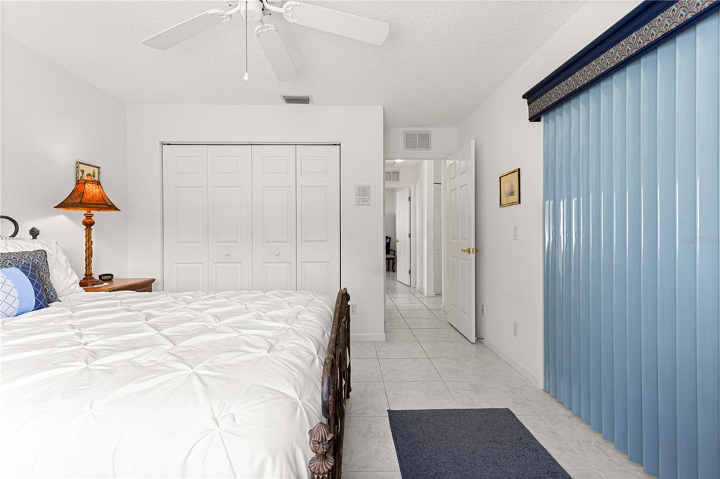 A bedroom features a white bed, tiled floors, a ceiling fan, and blue vertical blinds — 5292 NW 19TH PLACE, OCALA, FL
