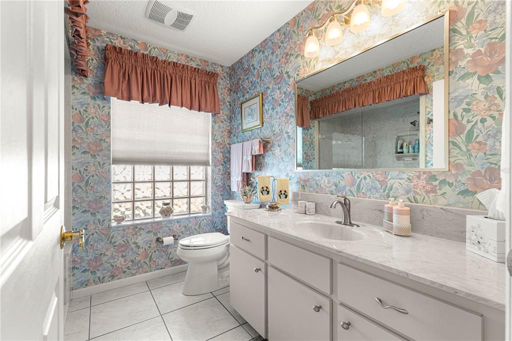A bathroom with floral wallpaper, a light gray vanity, a glass block window, and tile flooring — 5292 NW 19TH PLACE, OCALA, FL