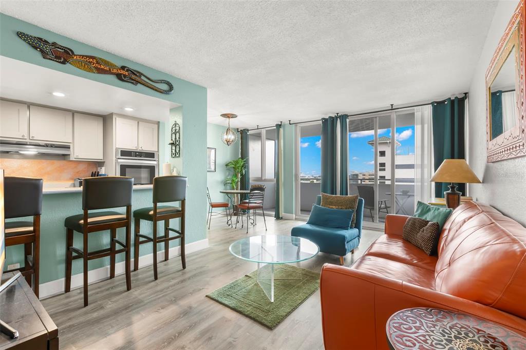 An open-concept living area features a kitchen with bar seating, a sofa, and balcony access — 470 3RD STREET S UNIT 613, ST PETERSBURG, FL