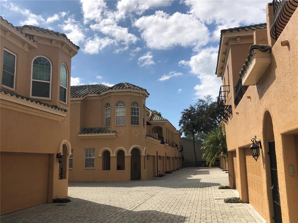 A paved driveway leads between two rows of tan stucco townhomes with arched windows — 2902 HANSEN MANOR LANE, TAMPA, FL