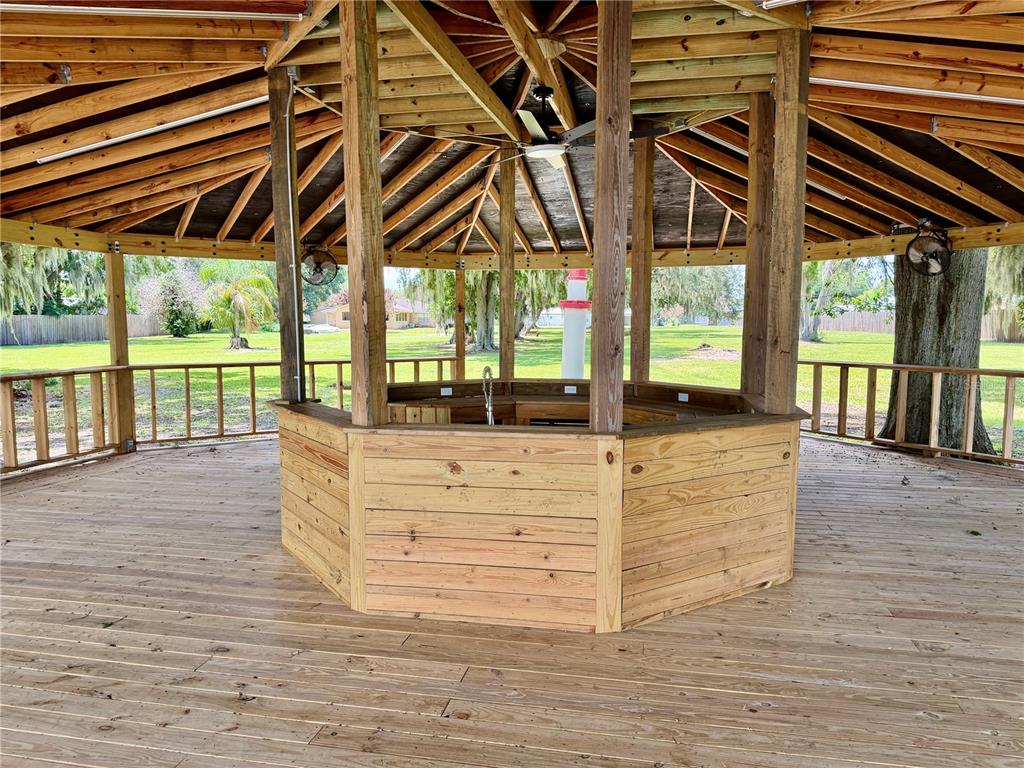 A grassy yard features a wooden gazebo and a decorative lighthouse near a lake — 1702 1/2 US HIGHWAY 92 W, AUBURNDALE, FL